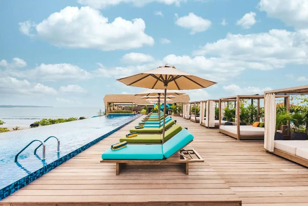 Rooftop-Terrasse im MAMAKA by Ovolo in Kuta mit Sonnenliegen, Sonnenschirmen, Pool und Meerblick über den Strand von Bali.