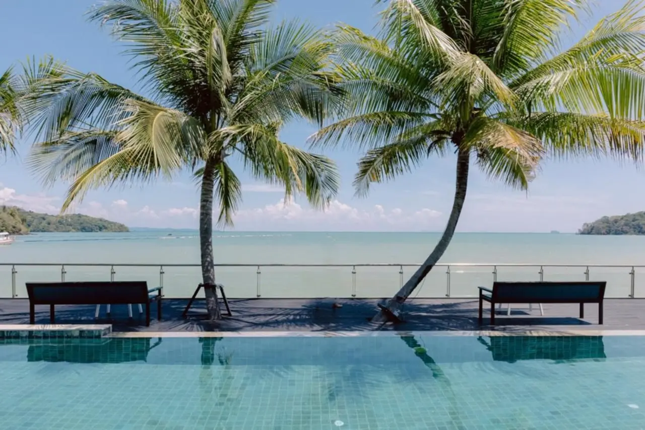 Blick über den Infinity-Pool des Hotel Tide Phuket Beachfront auf Palmen, Strand und Meer bei sonnigem Wetter