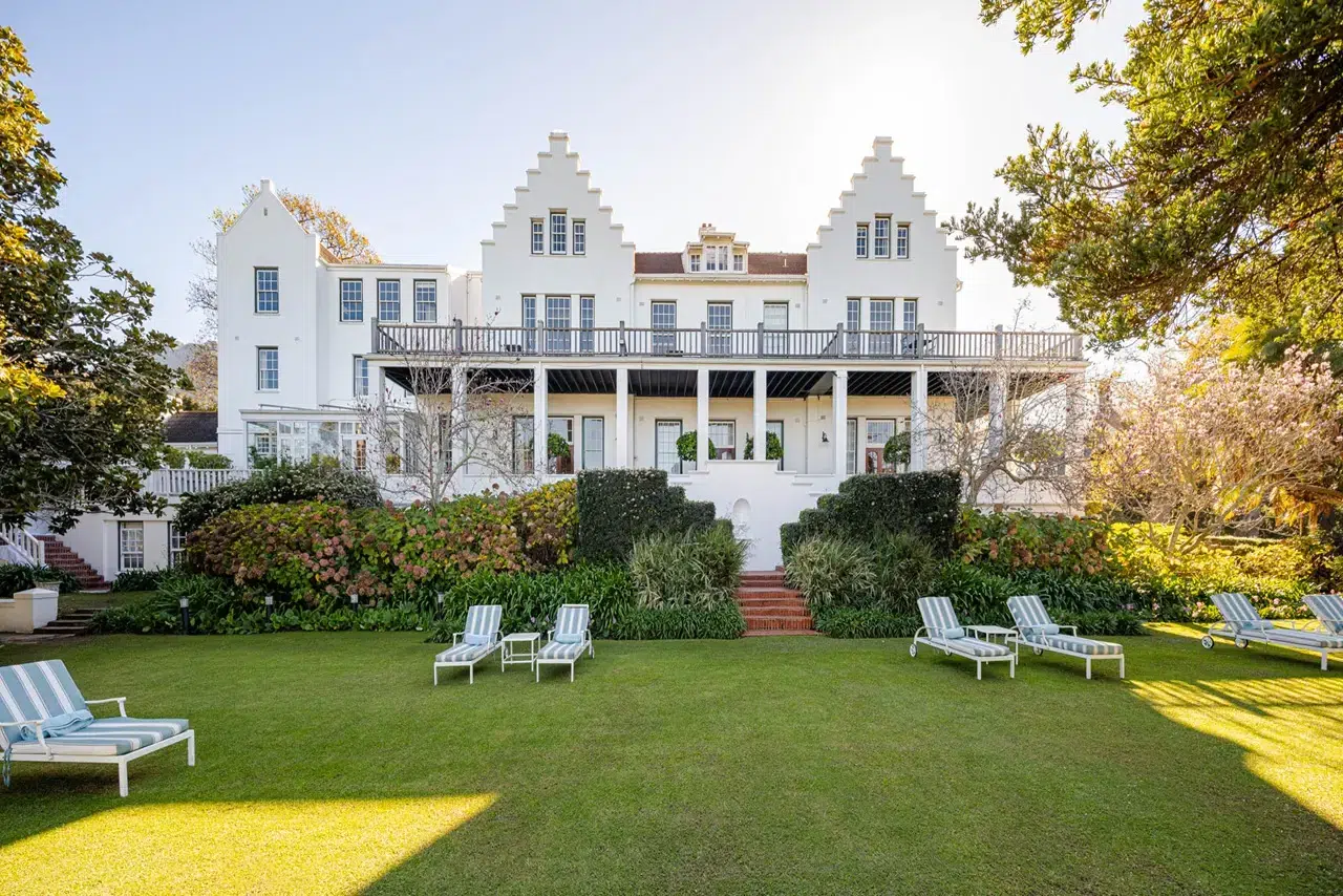 The Cellars-Hohenort Hotel bei Sonnenschein, mit gepflegtem Park und Sonnenliegen auf einer Wiese im Vordergrund.