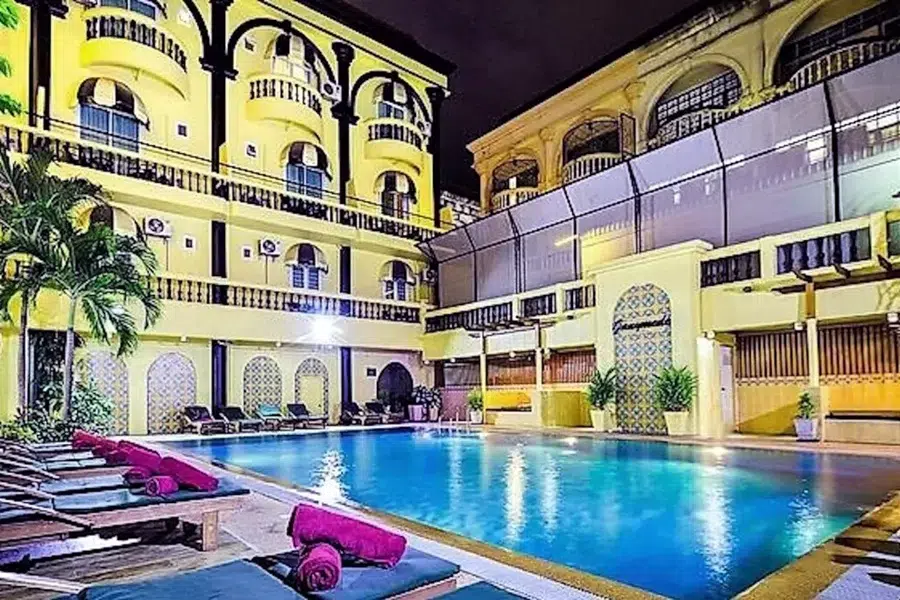 Illuminated pool in the Zing Resort & Spa Pattaya with high -quality loungers and hotel buildings in the evening